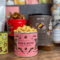 Can of 'Bob's Nuts Dilly Peanuts' with a pink label on a wooden surface, surrounded by other branded items.