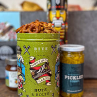 Tin of Nuts & Bolts with snacks and pickles on a wooden surface.