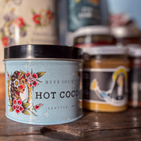 Bite Society hot cocoa container with other products on a wooden surface