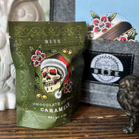 Green package of chocolate sea salt caramels with skull design on a wooden surface.