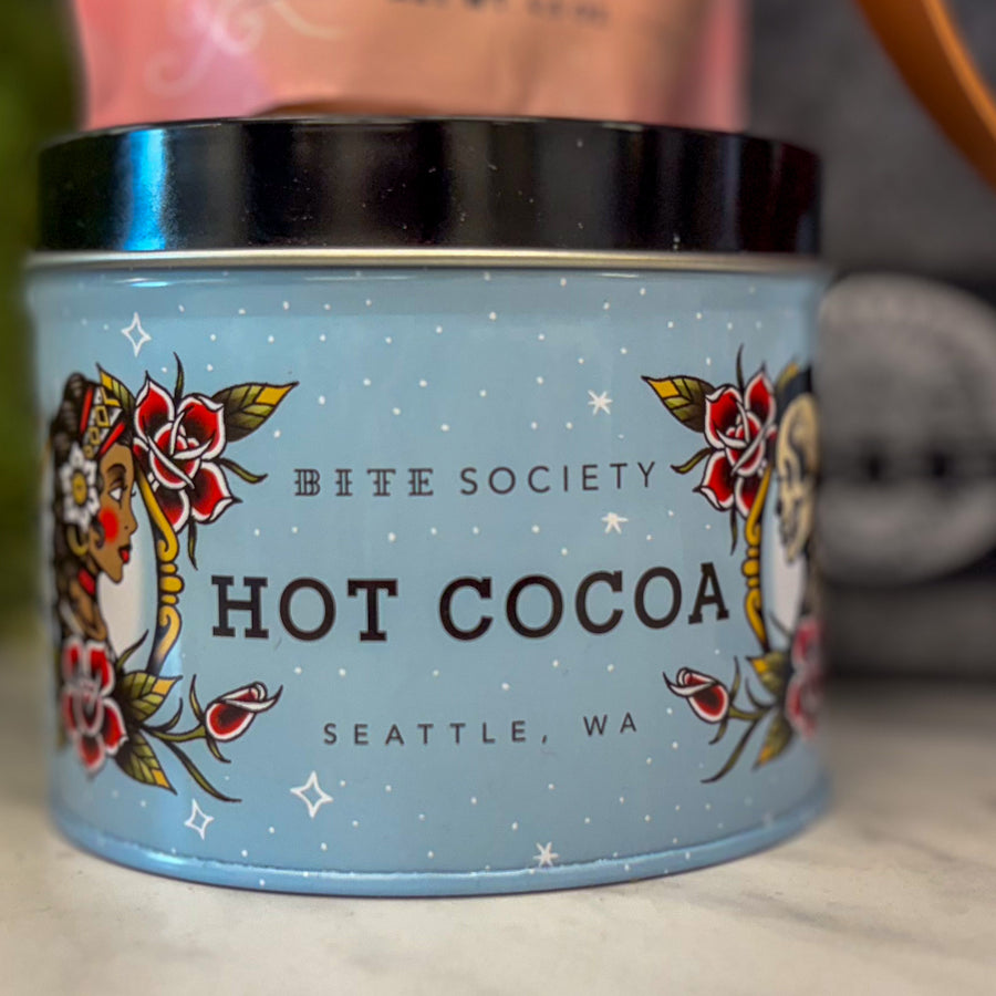 Bite Society hot cocoa container with decorative design on a blurred background