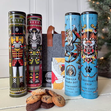 Four decorated cookie tins with illustrations of characters, a bag, and cookies on a surface.