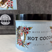 Bite Society hot cocoa canister with tattoo-style design on a blurred background