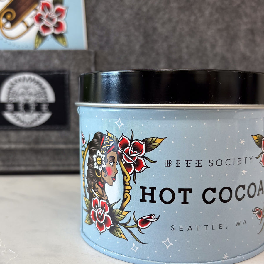 Bite Society hot cocoa canister with tattoo-style design on a blurred background