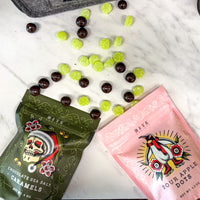 Two packs of candy, green bag of Caramels and pink bag of Sour Apple Dots, with scattered candies on a white surface.