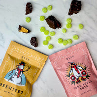 Two packages of Beehives and Sour Apple Dots on a marble surface with scattered candies.