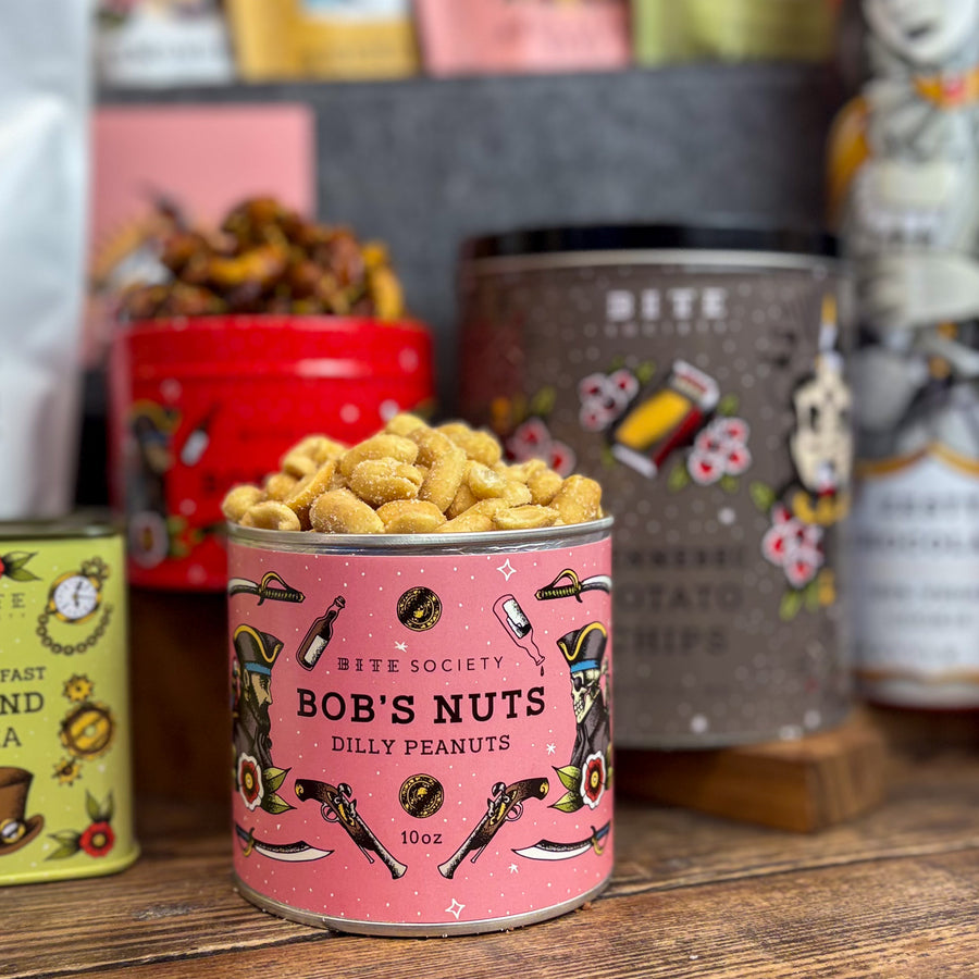 Can of 'Bob's Nuts Dilly Peanuts' with a pink label on a wooden surface, surrounded by other branded items.