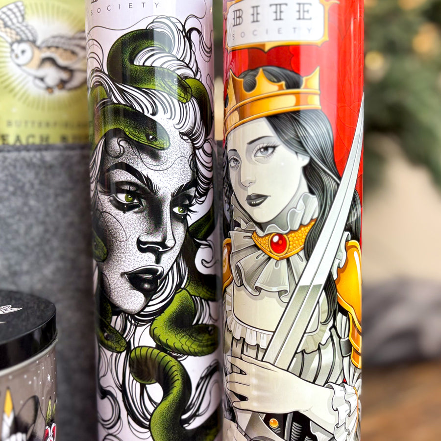 Two illustrated cookie tins with fantasy designs, one featuring Medusa the other the queen of swords on a blurred background.
