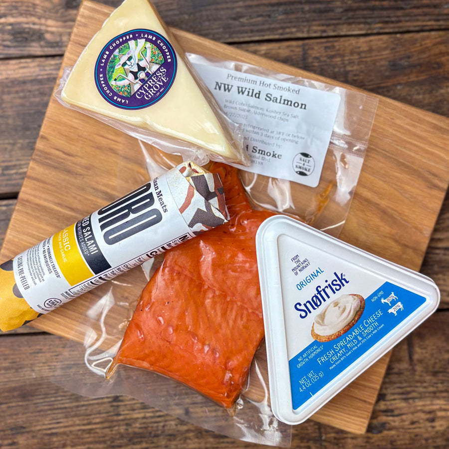 Cheese, salmon, and salami on a wooden cutting board.