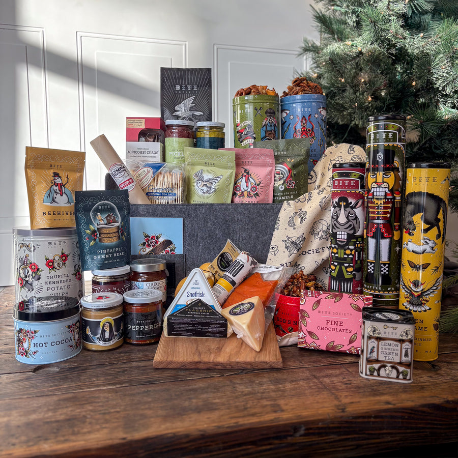 12 Days of Christmas Holiday Gift Basket with tins of cookies, cocoa, chips, and snacks. Along with bags of candy and a cooler of charcuterie and cheeses.