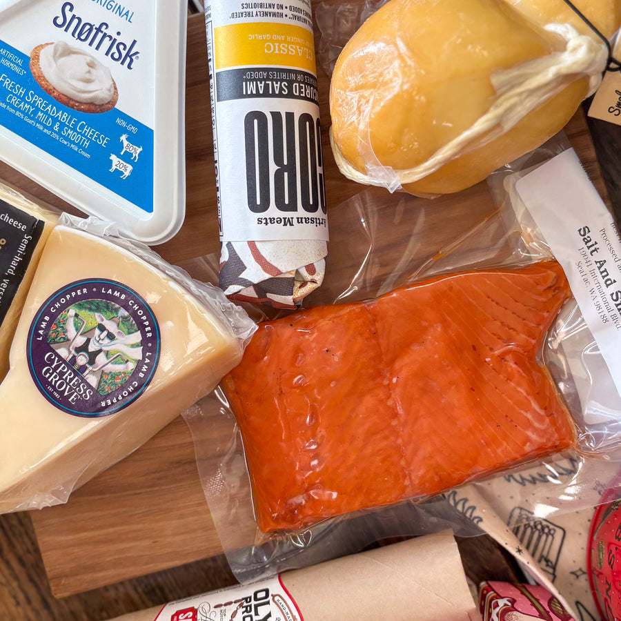 Assorted food items including cheese, salmon and salami on a wooden surface