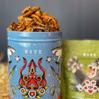 Blue tin container with snack mix and 'Bite Society' branding on a gray background